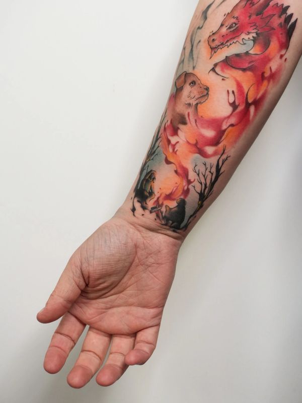 Colorful forearm tattoo featuring a dragon, a dog, and a campfire scene.