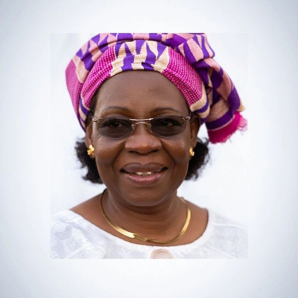 Smiling woman wearing glasses and a vibrant traditional headwrap.