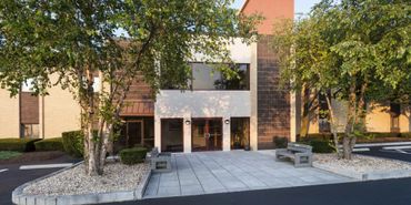 A modern building entrance with benches and trees on a sunny day.