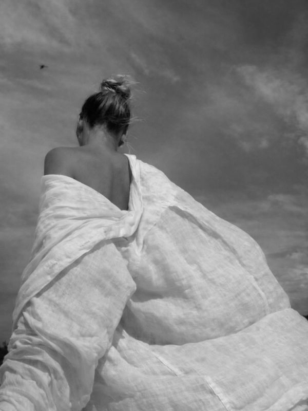 Woman wrapped in a flowing white fabric against a cloudy sky.