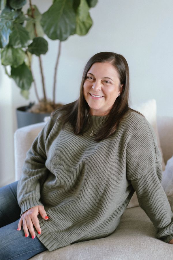 Woman smiling on a beige couch with a green sweater.