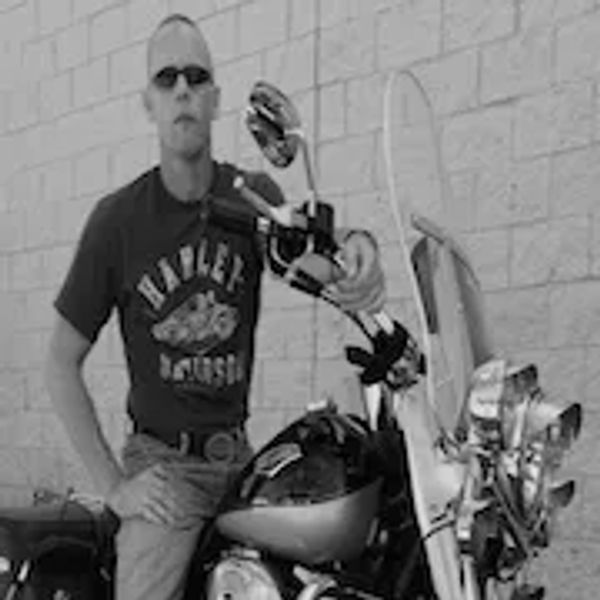 Man wearing sunglasses and a Harley-Davidson shirt sitting on a motorcycle.