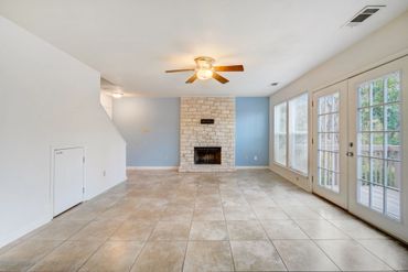 Bright living room with stone fireplace, tiled floor, and French doors.