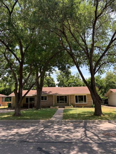 Single-story house with a red roof and large trees shading the front yard.