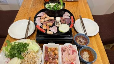 Korean BBQ setup with grill, marinated meats, vegetables, and dipping sauces on wooden table.
