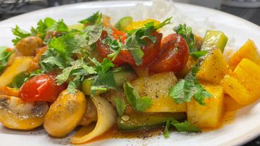 Colorful vegetable stir-fry with mushrooms, cherry tomatoes, bell peppers, and fresh herbs on a white plate.