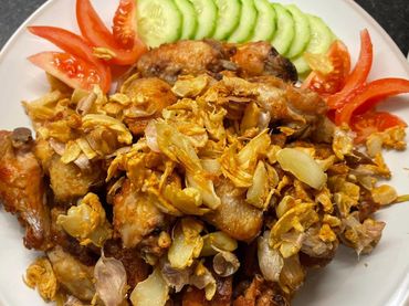 Plate of fried chicken wings topped with garlic, garnished with sliced cucumber and tomato.