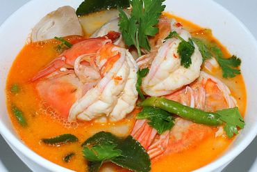 A bowl of spicy shrimp soup garnished with herbs and green chili.