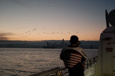Reinert Webb posing on SF ferry with city in Background and American flag jacket