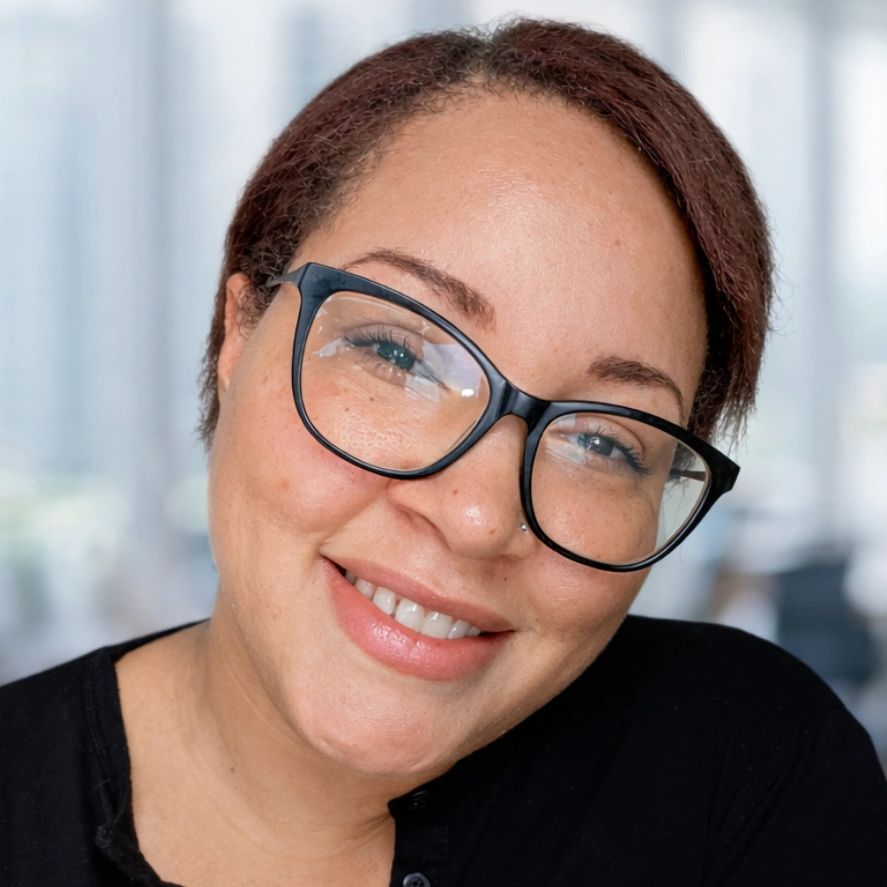 Smiling woman with glasses in a blurred office background.