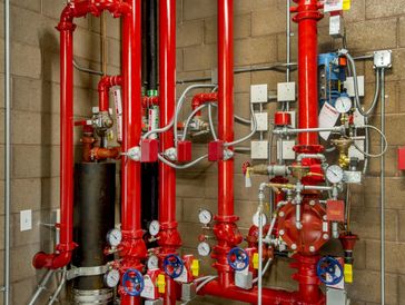 A network of red pipes and valves with pressure gauges on a concrete wall