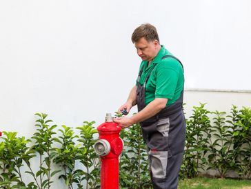 A person in a green shirt and work overalls is repairing a red fire hydrant