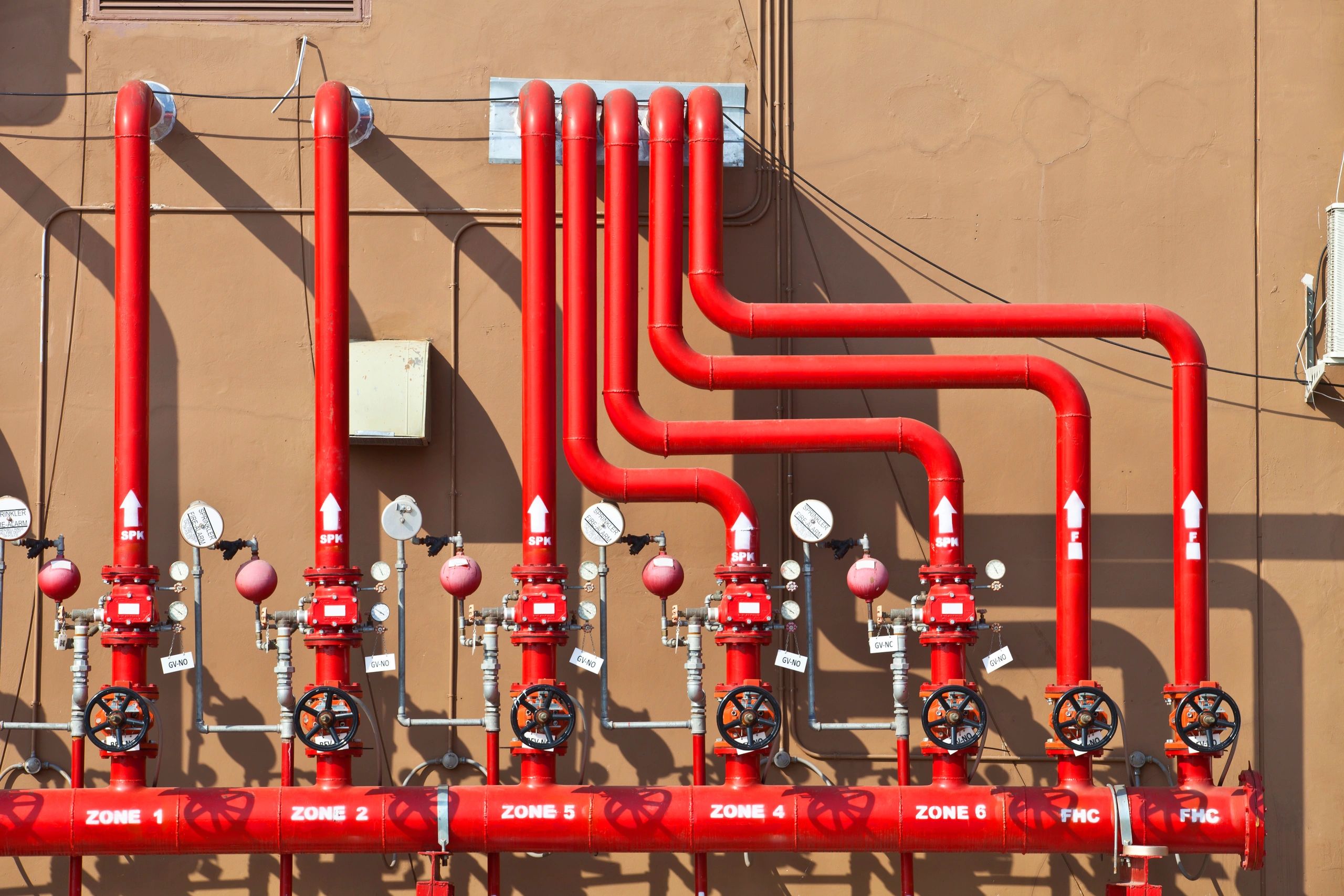 Red industrial piping with valves and pressure gauges labeled for different zones