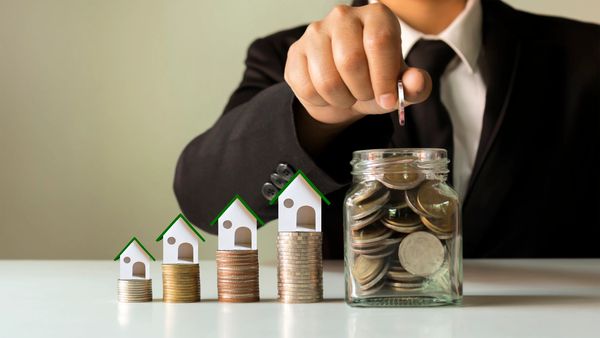 Hand holding coins in a jar for saving money and house designs on piles of coins
