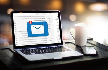 Laptop displaying a new email notification beside a phone and coffee cup.