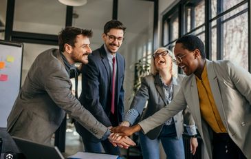 Four business colleagues smiling and stacking hands in teamwork gesture.