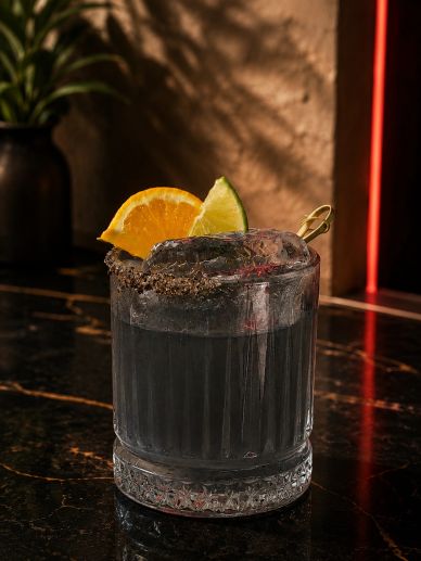 Dark cocktail with orange and lime garnish on a black marble table.