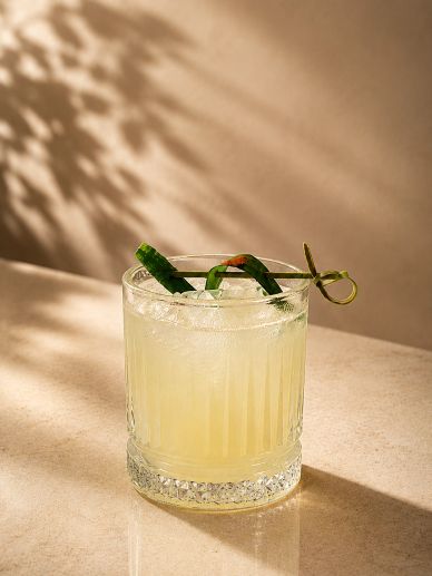 Refreshing cocktail with a cucumber garnish in a textured glass.