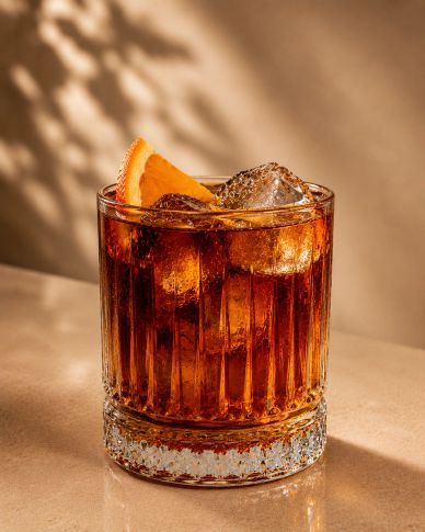 A glass of dark cocktail with ice and an orange slice garnish.