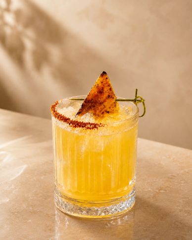 Refreshing yellow cocktail garnished with a chili-rimmed glass and grilled pineapple slice.
