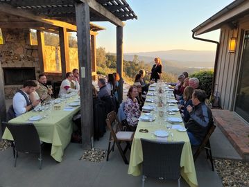 Outdoor dinner party with guests enjoying a sunset view over the hills.