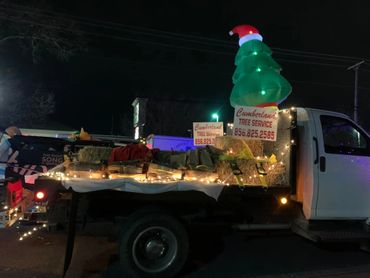 A decorated truck with Christmas lights and hay bales advertising Cumberland Tree Service at night.