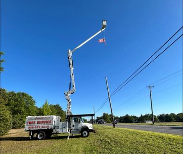 Tree service truck with extended boom holding a small American flag against a clear blue sky.