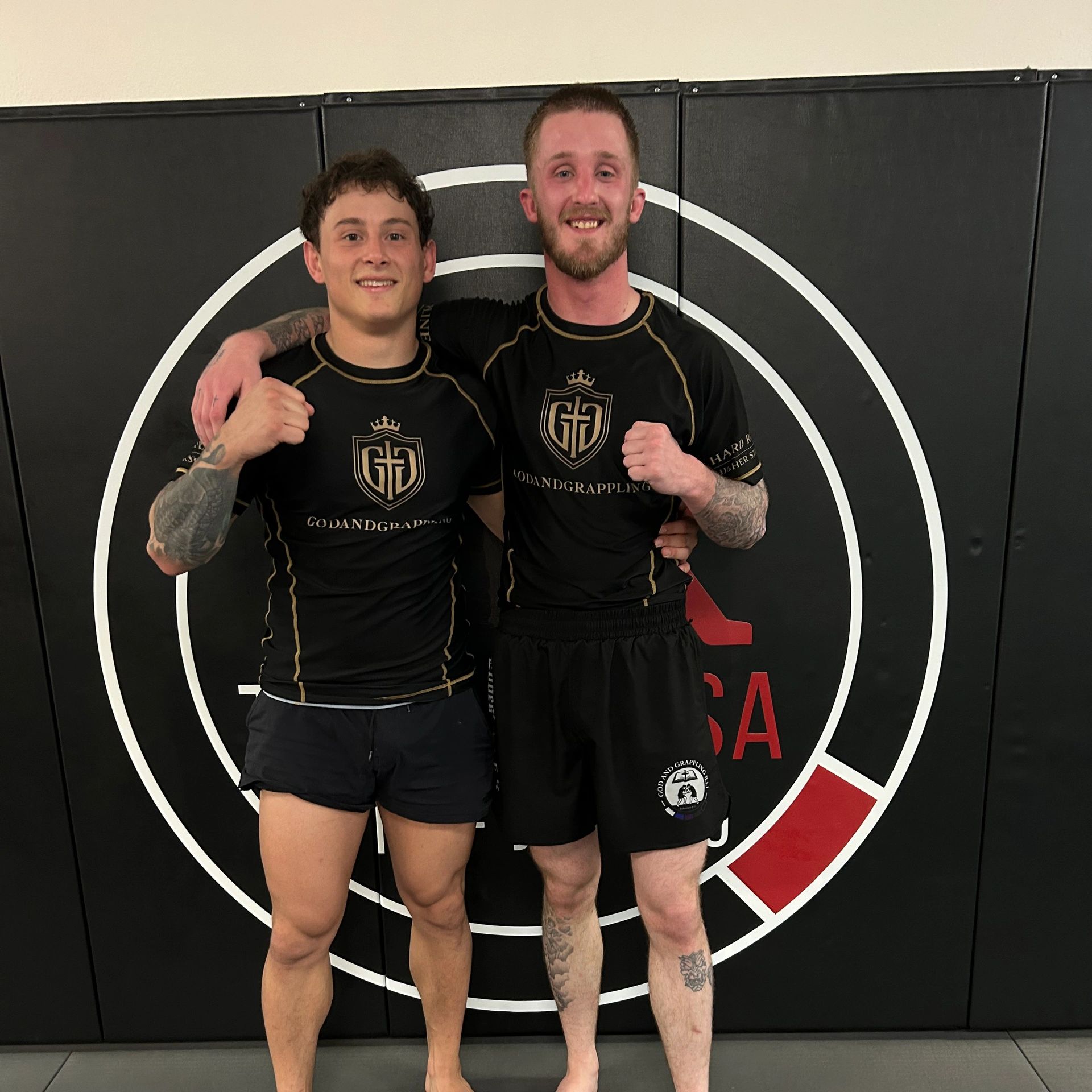 Two men in black grappling gear smiling and posing together.