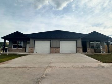 Modern duplex with two garage doors and a clean driveway under a cloudy sky.