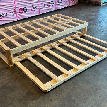 Two wooden bed frames stacked on a concrete floor in a warehouse.