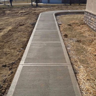 Newly poured concrete sidewalk curving around a building.