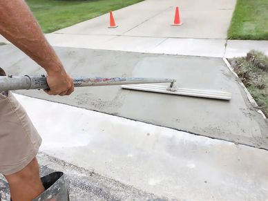 Person smoothing freshly poured concrete on a driveway section.