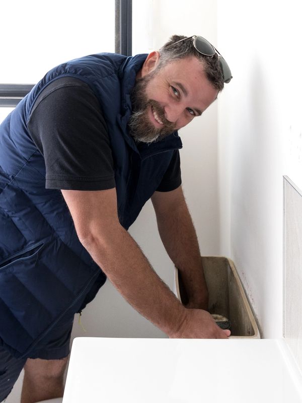 Smiling man fixing a toilet tank with sunglasses on his head.