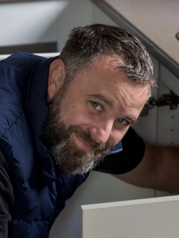 Man with beard smiling while fixing kitchen cabinet.