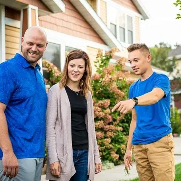 Three people standing outside a house, one pointing at something.