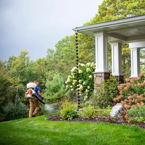 Person using a blower to clean the lawn near a porch.