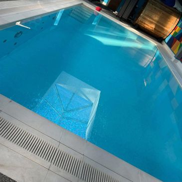 Indoor swimming pool with clear blue water and tiled steps.
