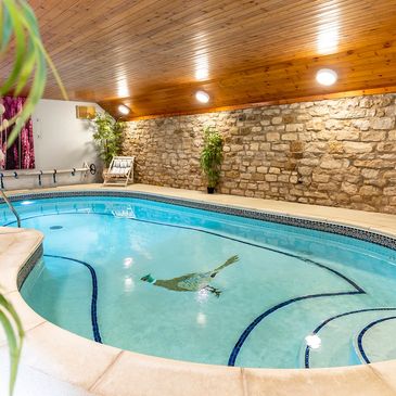 Indoor swimming pool with stone wall and wooden ceiling.