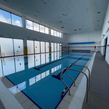 Indoor swimming pool with clear water and large windows letting in natural light.