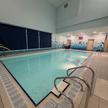 Indoor swimming pool with tiled floor and blue chairs along the wall.