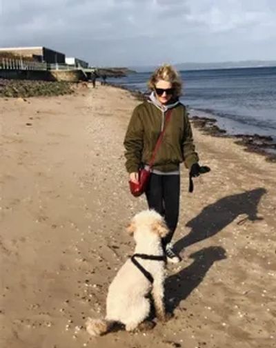 A woman, walking her dog on the beach.
