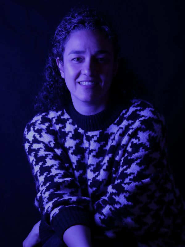 Portrait of a smiling woman in a patterned sweater under blue lighting.