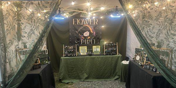 A cozy, witchy inspired jewelry booth with green and black decor and string lights.