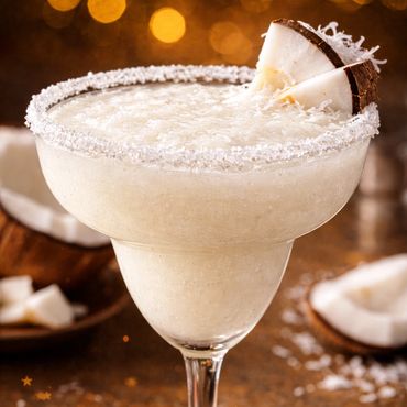 Creamy coconut cocktail garnished with coconut slices and rimmed with shredded coconut.
