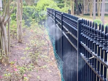 Garden sprinkler watering plants along a black fence.