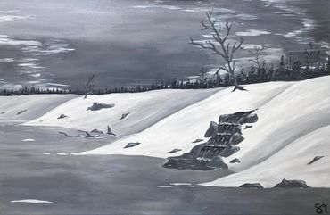 A black and white landscape in a winter setting with distant trees, snow cover rocks, and a creek.
