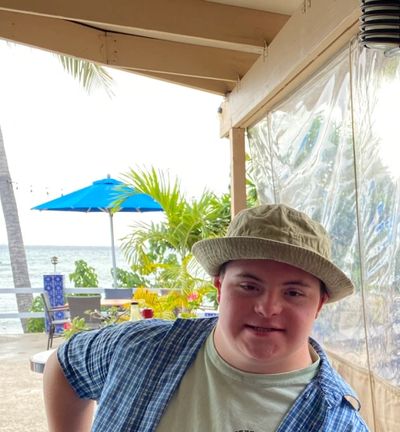 Young man in a hat smiling at a beachside café.