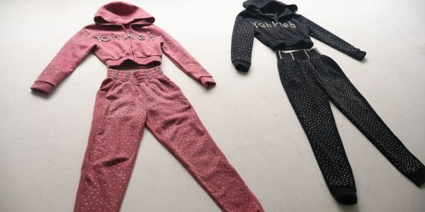 Two glittery sweat suits, one pink and one black, laid flat on a white surface.