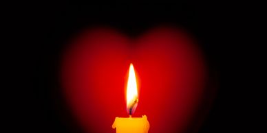 A glowing candle flame with a heart-shaped red light in the background.