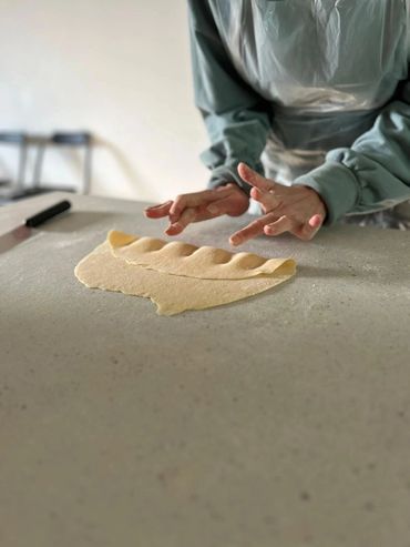Hands shaping dough on a kitchen counter, preparing homemade pasta or dumplings.